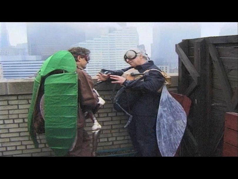 Two artists, one dressed as a beetle the other as a fly, converse