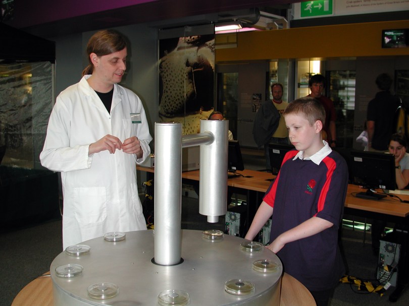 Man in white coat shows petri dishes of bacteria on release device to young boy