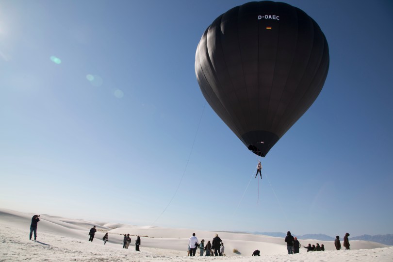 black balloon, person suspended, white desert, blue sky