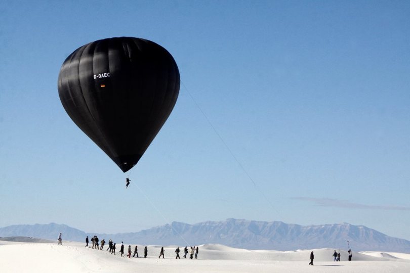 black balloon, person suspended, white desert, blue sky