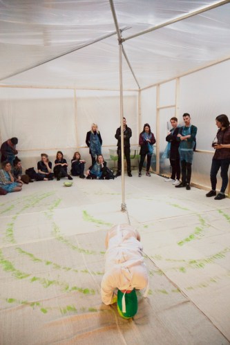 Man paints spiral of green paint with his head in enclosed performance space