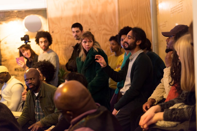 An audience in a small room look at a person making a point with interest.