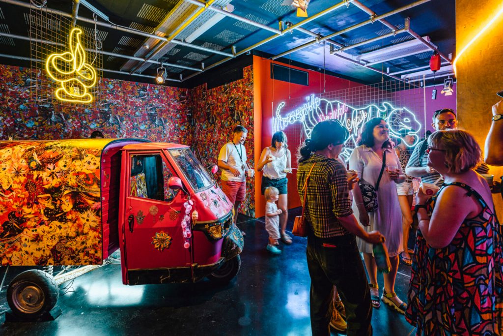 Groups of people talk within a visually rich, neon-bedecked installation.